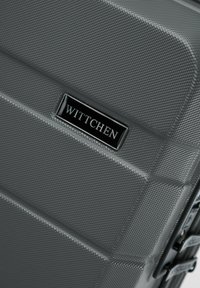 Šedý tvrdý kufr s texturovaným povrchem a diagonálními žebrováními, s černou kovovou značkou "WITTCHEN" na přední straně.