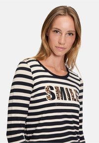 Schwarz-weißer gestreifter Langarmshirt mit rundem Ausschnitt und dem Wort "SMILE" im Leopardenmuster, darunter zusätzlicher Text.