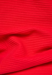 Red textured fabric with a ribbed pattern, featuring soft folds. The surface is smooth, highlighting the vibrant color and vertical lines.