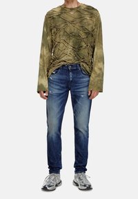Olive green long-sleeve shirt with cut-out design, paired with blue distressed jeans and silver sneakers. Visible stitching and texture details.