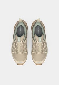 Ténis atléticos bege com parte superior em malha, colarinho acolchoado e acentos em verde claro contrastantes. Apresenta uma sola texturizada para aderência e estabilidade.