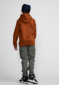 Oranje hoodie, groene cargobroek, zwarte hoge sneakers, eenvoudig ontwerp, zichtbare stiksels, ontspannen pasvorm, geschikt voor casual wear.