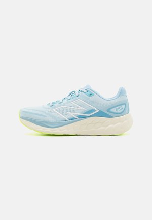 Zapatilla deportiva de color azul claro con parte superior de malla texturizada, acentos blancos y una suela acolchada color crema con un toque de neón amarillo.