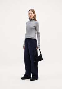 Grauer Reißverschluss-Pullover, marineblaue weite Cordhosen und schwarze Handtasche. Einfaches Design mit strukturiertem Stoff und lockerer Passform.
