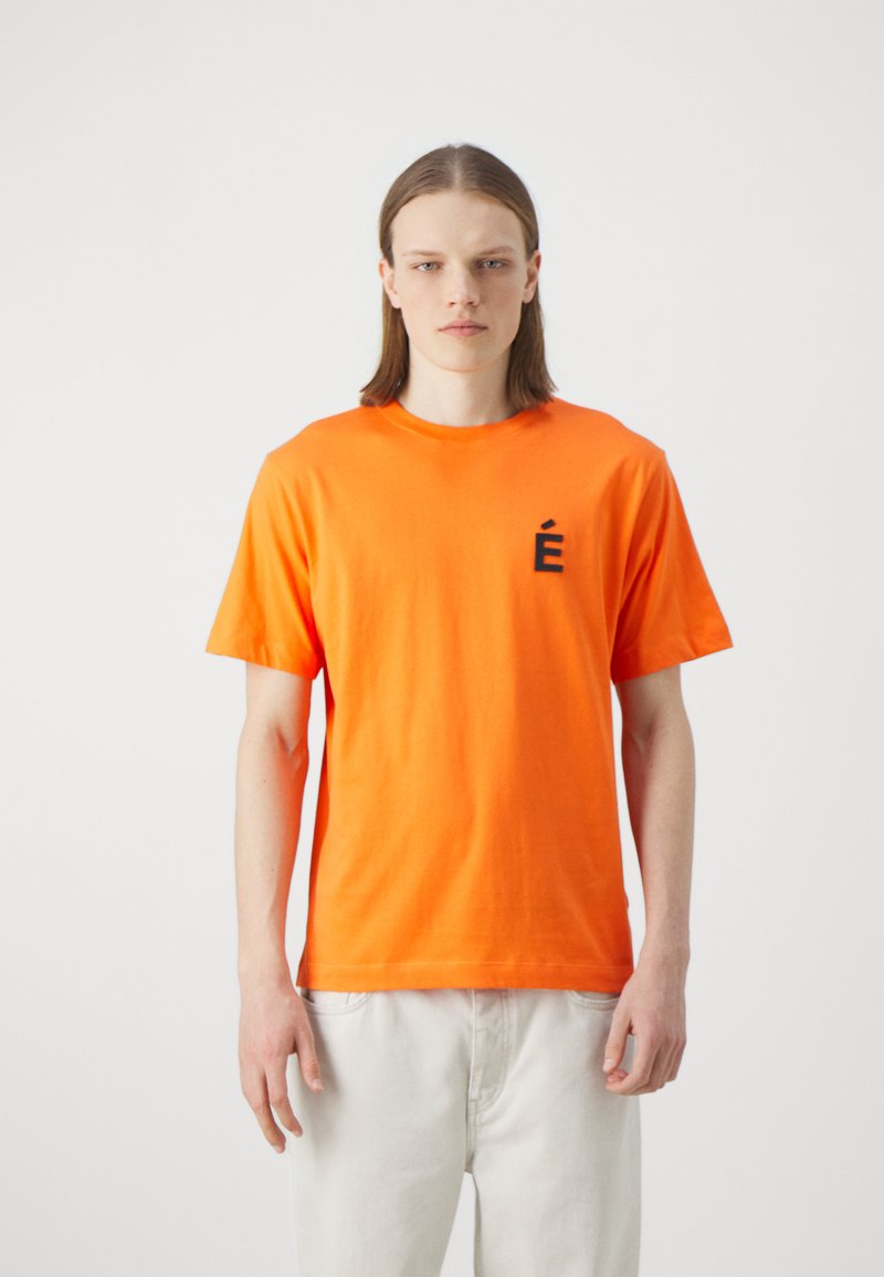 Orange cotton t-shirt featuring a round neckline and short sleeves. Black embroidered "É" logo on the left chest area. Plain design.