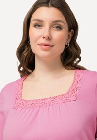 Top rosa con scollo quadrato e dettagli in pizzo. Il tessuto è morbido e leggero, progettato con una vestibilità comoda e leggere arricciature.