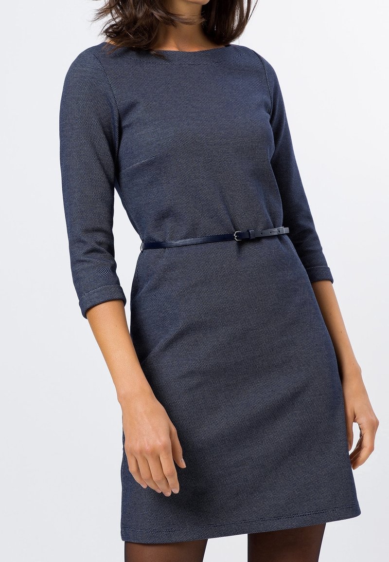 Tmavě modré šaty s tříčtvrtečními rukávy, vypasovaným pasem a tenkým odpovídajícím pásem. Texturovaná látka s jemným vzorem.