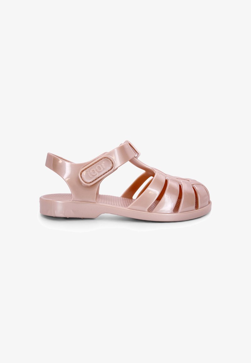 Sandale en plastique rose pâle à bout fermé, côtés ajourés, bride à la cheville et semelle plate, montrée de profil sur fond blanc.