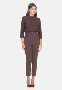 Camicia bordeaux con due tasche anteriori, colletto a bottoni e maniche arrotolate; pantaloni a vita alta coordinati con dettagli zip; tacchi a punta bordeaux.