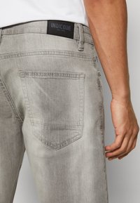 Gray denim jeans featuring a back pocket and a black brand label, showcasing a smooth texture and a modern cut.