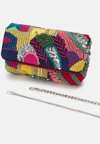 Bolso de mano colorido con lentejuelas, cuentas y patrones geométricos bordados, acompañado de dos correas de cadena plateadas desmontables sobre una superficie blanca.