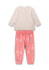 Helle beige Langarmoberteil kombiniert mit rosa Jogginghosen, die ein Muster aus bunten Giraffen aufweisen. Hergestellt aus weichem Baumwollstoff.