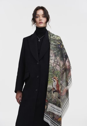 Wool scarf featuring a fox and nature scene in vibrant colors, draped over a black coat, with a delicate fringe and striped border.