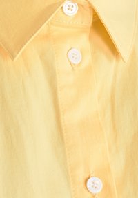 Primo piano di un colletto di camicia giallo con una chiusura a bottoni che presenta tre bottoni bianchi e dettagli di cucitura visibili.