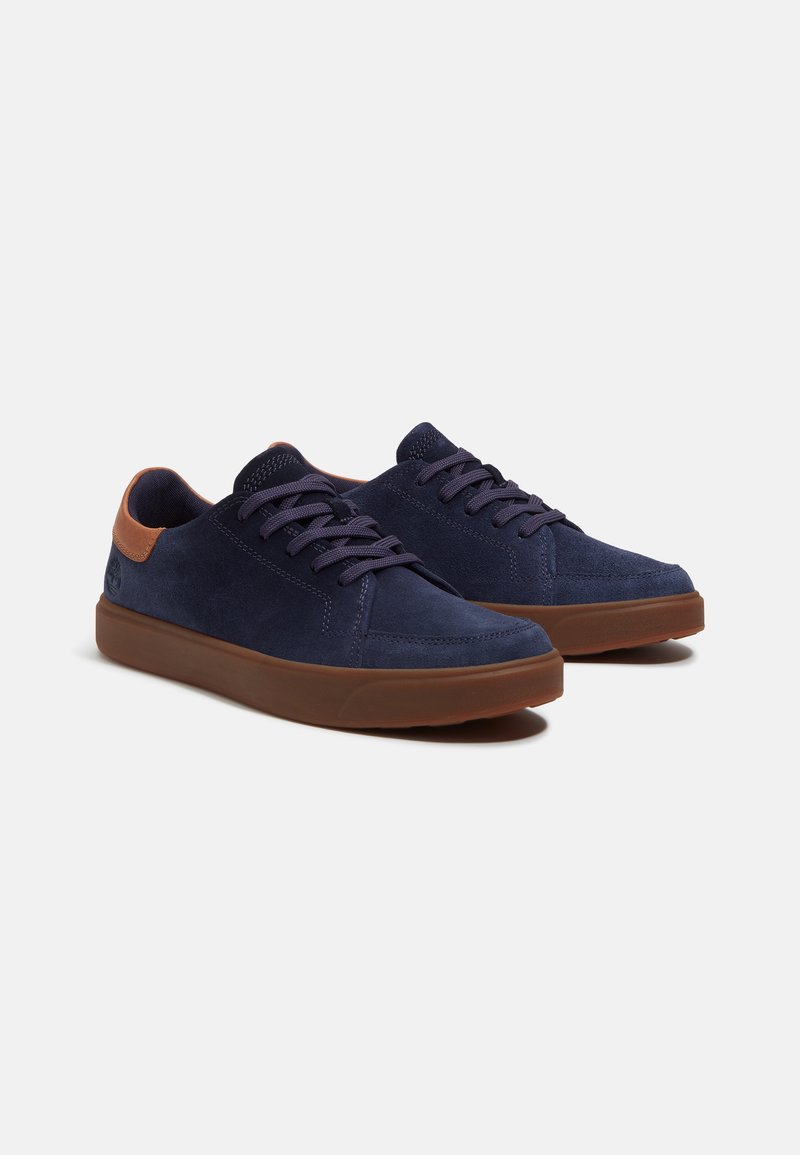 Sneakers in suede blu navy con accenti in pelle marrone, punta tonda e suola in gomma piatta. Presentano lacci coordinati e dettagli di cucitura sottili.