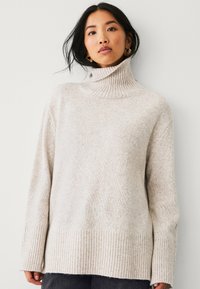 Maglione a collo alto grigio chiaro in un morbido knit testurizzato. Presenta un collo e un orlo a costine con maniche lunghe e morbide.