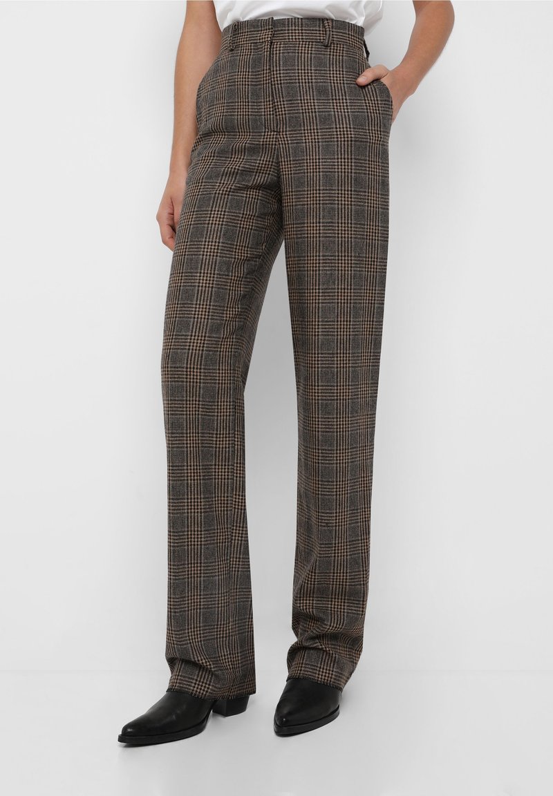 Pantalons à carreaux marron avec taille haute, jambes droites et poches latérales, en tissu texturé, associés à des bottines noires.