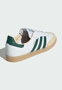 Sneakers bianchi in pelle con strisce e dettagli verdi. Presentano una suola in gomma testurizzata color sabbia e una punta in suede. Testo "SAMBA" sul lato.