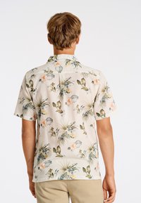 Camisa de manga corta de flores hecha de tejido ligero; presenta un fondo beige con hojas verdes y flores melocotón; corte casual y relajado.