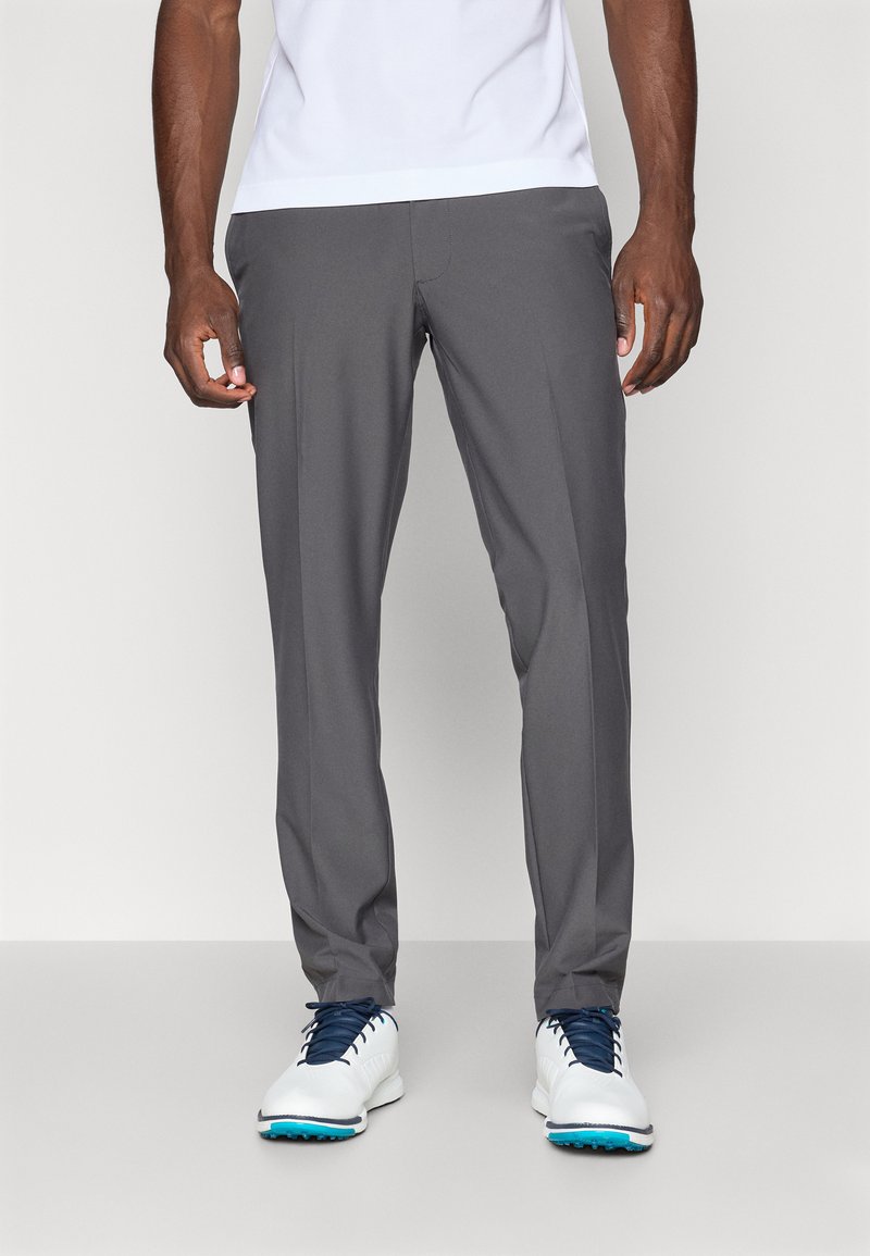 Gray athletic trousers with a smooth texture, tapered fit, and crease detail. Paired with white sneakers featuring blue accents.