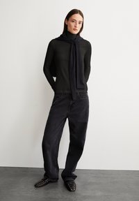 Zwarte lange mouwen top gecombineerd met losse zwarte jeans en zwarte studied schoenen. Een donkere sjaal hangt om de nek en creëert een gelaagd uiterlijk.