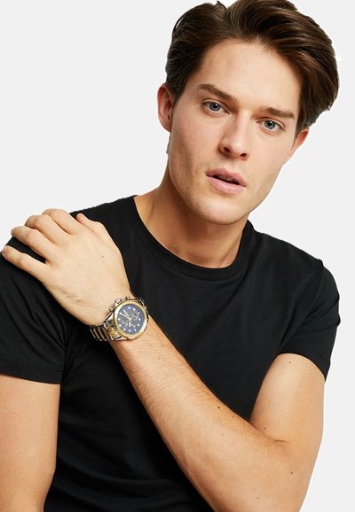 Montre-bracelet en or et en argent avec un cadran bleu foncé, dotée d'un bracelet en acier inoxydable, d'accents de chronographe et d'un design de boîtier rond.