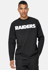 Svart långärmad T-shirt i bomull, med en stor vit "RAIDERS"-grafik på framsidan. Rundad nacke och avslappnad passform.