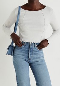 Top de manga larga blanco acanalado con dobladillo festoneado, combinado con jeans de tiro alto de color azul claro. Un pequeño bolso azul cuelga del hombro.