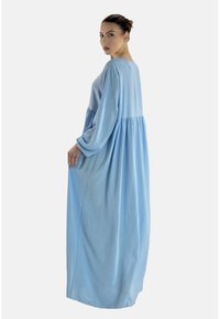Jasnoniebieska długa sukienka z miękkiego, fakturowanego materiału, o luźnym kroju, długich rękawach i zebranej talii dla uzyskania objętości.