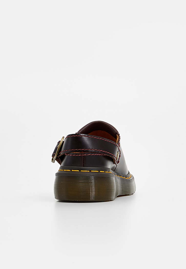 Zapato de cuero marrón oscuro con un tacón bajo, que presenta una correa y un detalle de hebilla; costuras amarillas en contraste a lo largo de la suela.