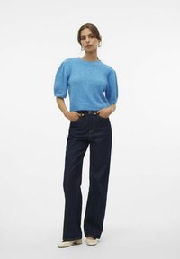 Maglione a maglia blu chiaro, a maniche corte, con scollo rotondo. Abbinato a jeans a gamba larga blu scuro e scarpe chiare. Design semplice.