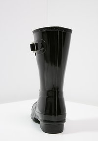 Bottes de pluie noires en caoutchouc avec une finition brillante, hauteur mi-mollet, dotées d'une sangle latérale décorative et d'une semelle texturée pour une meilleure adhérence.