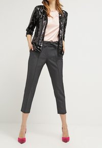 Musta paljettitakki vaaleanpunaisen topin päällä, yhdistetty harmaisiin kapeneviin housuihin ja vaaleanpunaisiin korkokenkiin. Sileät materiaalit kiiltävillä yksityiskohdilla.