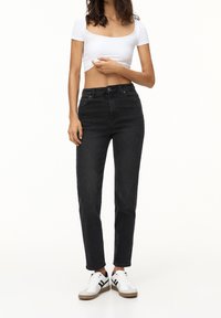 Černé vysoce pasové džíny s rovnými nohavicemi, vyrobené z denimu. Nosí se s bílým cropped topem a bílými teniskami s černými detaily.