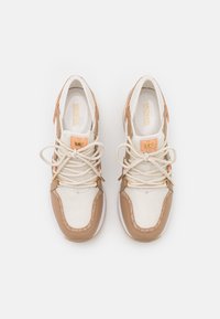 Sneaker con un mix di mesh bianco e pelle sintetica beige, con accenti del logo dorati, lacci piatti e una suola texturizzata.