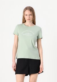T-shirt en coton vert clair à manches courtes et col rond. Présente un texte blanc disant "RIEN DE TEL QUE CE MAGNIFIQUE JOUR D'ÉTÉ."