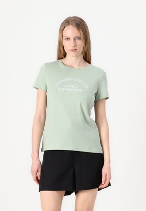 T-shirt en coton vert clair à manches courtes et col rond. Présente un texte blanc disant "RIEN DE TEL QUE CE MAGNIFIQUE JOUR D'ÉTÉ."