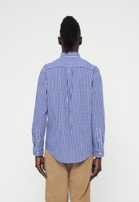 Μπλε και λευκό πουκάμισο με κουμπιά, μακριά μανίκια, λεπτομέρεια στο πίσω μέρος και στρογγυλεμένη ραφή. Το ύφασμα φαίνεται ελαφρύ και λείο.