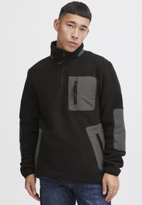 Fleecepullover in Schwarz mit grauen Akzenten. Verfügt über einen halben Reißverschluss, eine Brusttasche mit Reißverschluss und seitliche Taschen für Stauraum.