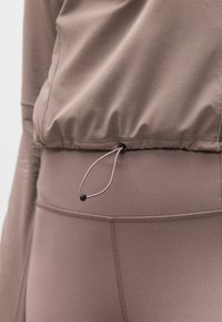 Κοντινό πλάνο σε ενεργειακά ρούχα σε απόχρωση ταουπ, με ρυθμιζόμενο κορδόνι στη μέση και υφασμένο σχέδιο ραφής στα κολάν.