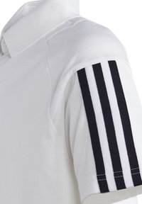 Biała koszulka polo z teksturowanego materiału, klasycznym kołnierzykiem i trzema czarnymi pionowymi paskami na rękawie.