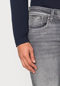 Grå denimjeans med klassisk passform, som har en sidoficka och subtila sömnadsdetaljer, parat med en marinblå långärmad topp.