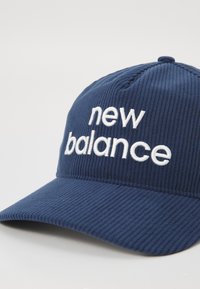 Marineblå cordfløyelslue med buet skygge og hvit brodert "new balance"-logo på frontpanelet.