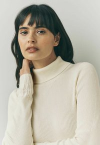 Cremefarvet ribbet turtleneck sweater med lange ærmer, der har et struktureret mønster ved manchetterne og en tætsiddende silhuet.