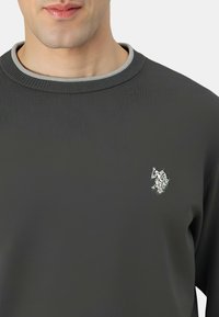 Maglione a maniche lunghe di colore grigio scuro con trama a coste e colletto a contrasto grigio chiaro. Presenta un piccolo logo ricamato sul petto.