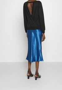 Haut noir à manches longues avec un dos en V profond. Assorti à une jupe midi en satin bleu, avec un ourlet évasé et une texture lisse. Talons noirs.