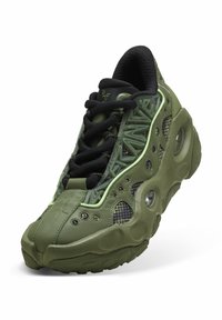 Chaussure de sport verte et noire avec une semelle épaisse, des détails en mesh, un laçage à l'avant et des panneaux latéraux texturés avec un motif et un logo.