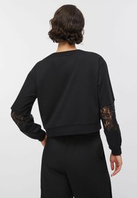 Sweat-shirt noir court avec manches longues en dentelle, doté d'un col rond et d'une ceinture élastique, conçu pour une coupe ample.