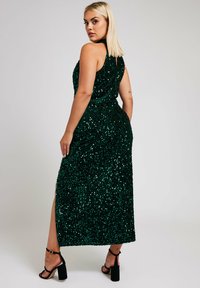 Grön paljettmaxiklänning med hög slits, ärmlös design och mjuk textur. Klänningen har en figurnära silhuett och glittrar i ljuset.