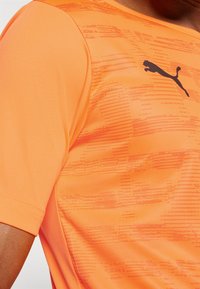 Kurzes, sportliches T-Shirt mit Rundhalsausschnitt in leuchtendem Orange, das strukturierte Linien und ein schwarzes Puma-Logo auf der linken Brust aufweist.